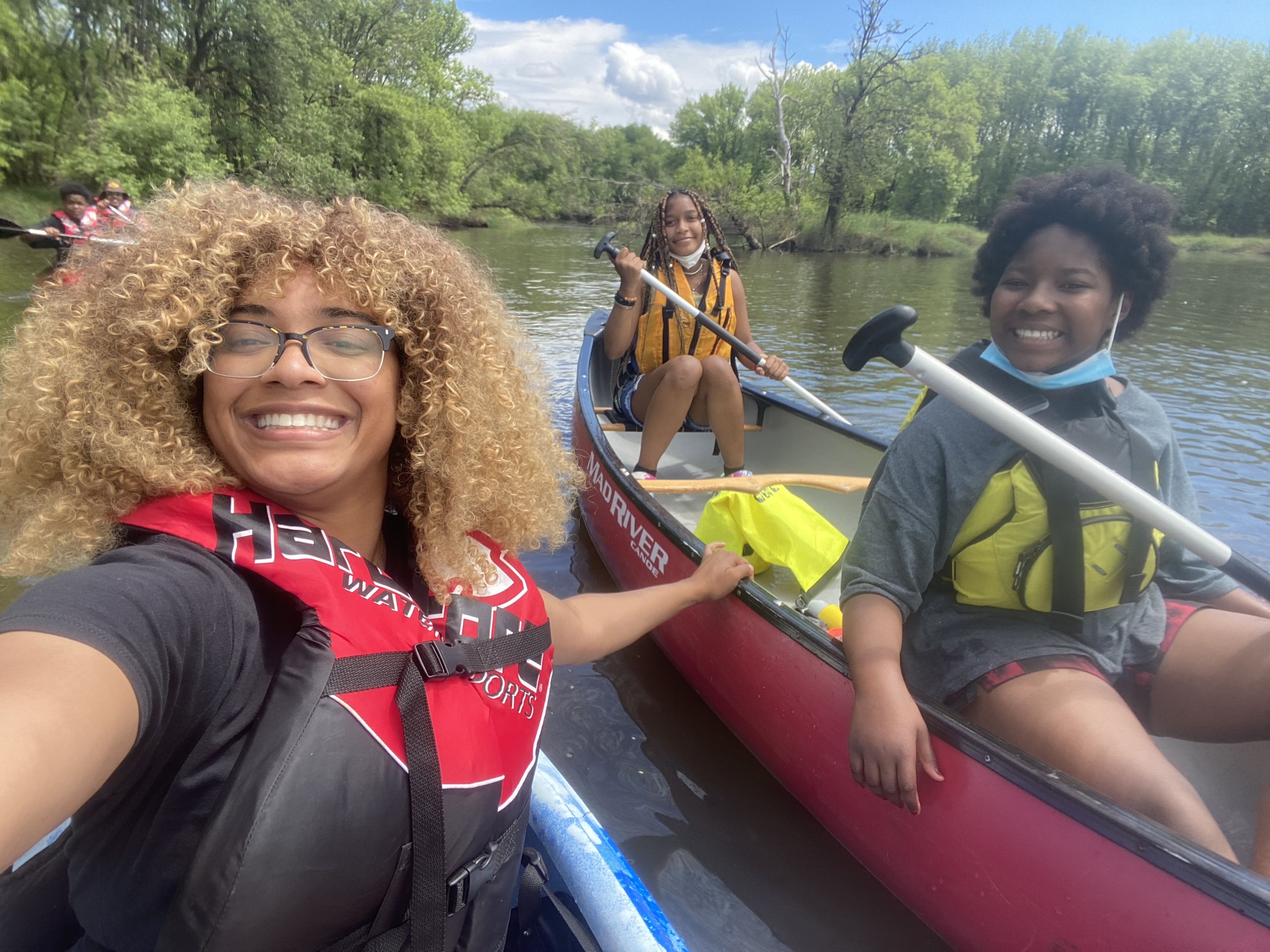 Three people sit in canoes and smile at the camera
